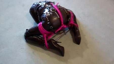 Adreena Booted Hooded And Straitjacketed  2 - In the second part of this video clip, adreena is still dressed from head to toes in fetish clothing. A severe pvc hood with a pink ballgag tops an outfit consisting of a heavy rubber straitjacket, rubber capri pants and thigh high corset boots.

a steel spreader bar is attached to adreena's ankles and pink ropes are added to the bondage to make it progressively harder for adreena to move around the floor.  Adreena does not enjoy being treated this way!
