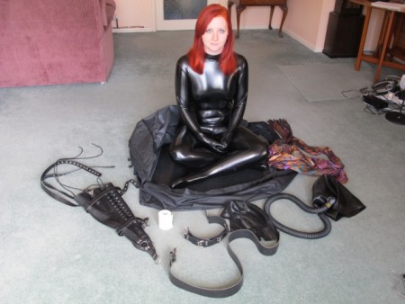 Karina Prepared For Transport - This is the first of two parts where we see karina, dressed in two catsuits and two hoods, prepared for transportation for further training.  A long hose is attached to her rubber narcosis hood, followed by a leather armbinder.