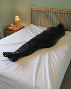 Under Five Layers  Part 1 - In this first of two parts, karina is encased in four layers.
first a black spandex zentai suit over which she pulls two pairs of pantyhose - one for the bottom and one for the top part of her body.
then she adds a shiny pvc hood and waits for the brown parcel tape to be wrapped around her body.
the clip then concludes by showing how she is encased in the neck-entry rubber sleepsack.  The final layer and a further hood is added in the second part of the clip.